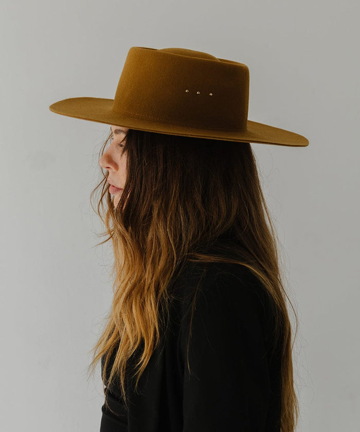 Woman wearing a cinnamon colored boater hat and a black coat, facing sideways against a plain background #color_cinnamon