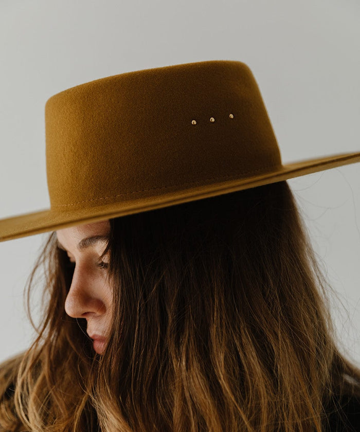 Woman wearing a cinnamon colored boater hat, looking sideways against a plain background #color_cinnamon
