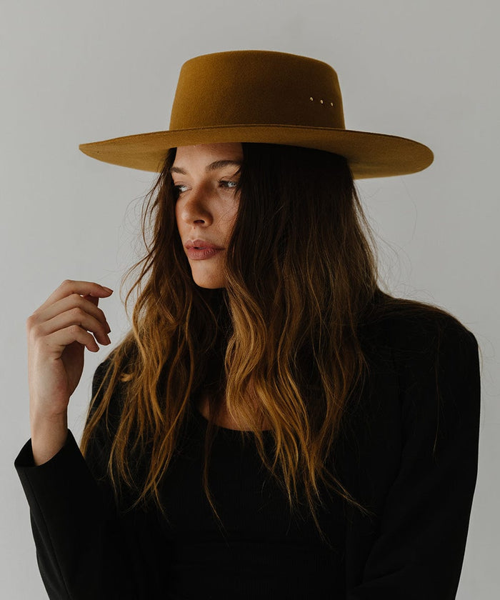 Woman wearing a cinnamon colored boater hat and a black coat, posing against a plain background #color_cinnamon