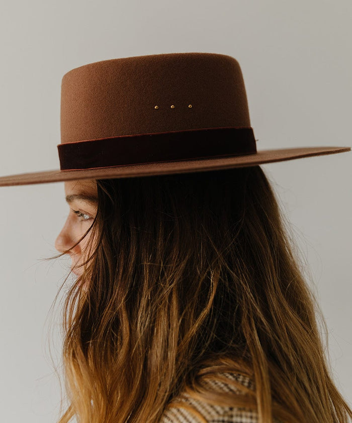 Woman wearing a cinnamon colored boater hat with a hat band, facing sideways against a plain background #color_cinnamon