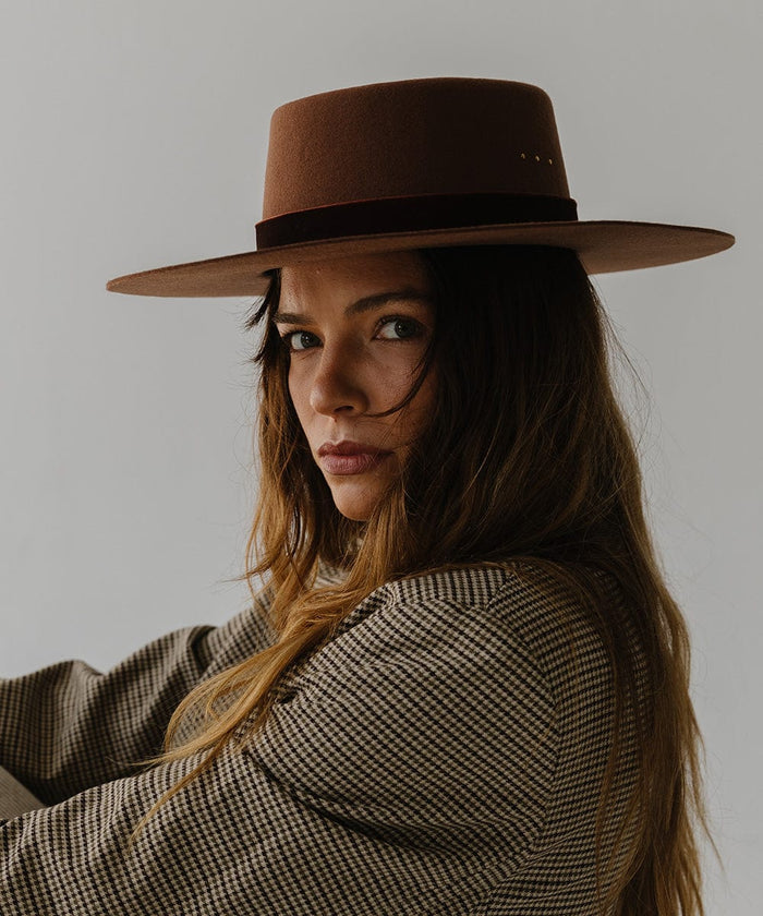 Woman wearing a dark oak colored boater hat with a hat band and a coat, posing against a plain background #color_dark oak