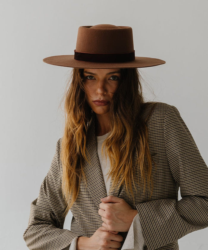 Woman wearing a dark oak colored boater hat with a hat band and a coat against a plain background #color_dark oak