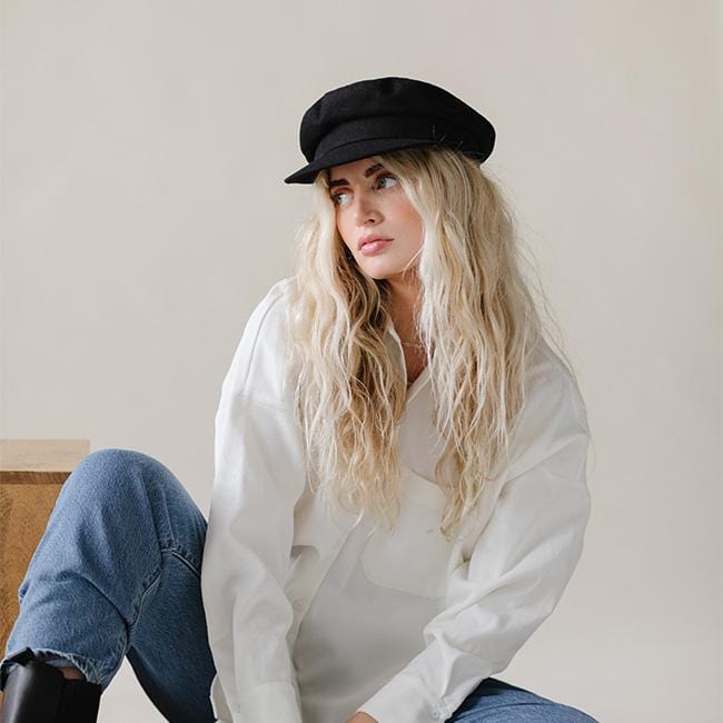 Woman wearing a black cap, a white shirt and blue jeans, sitting against a plain background #color_black