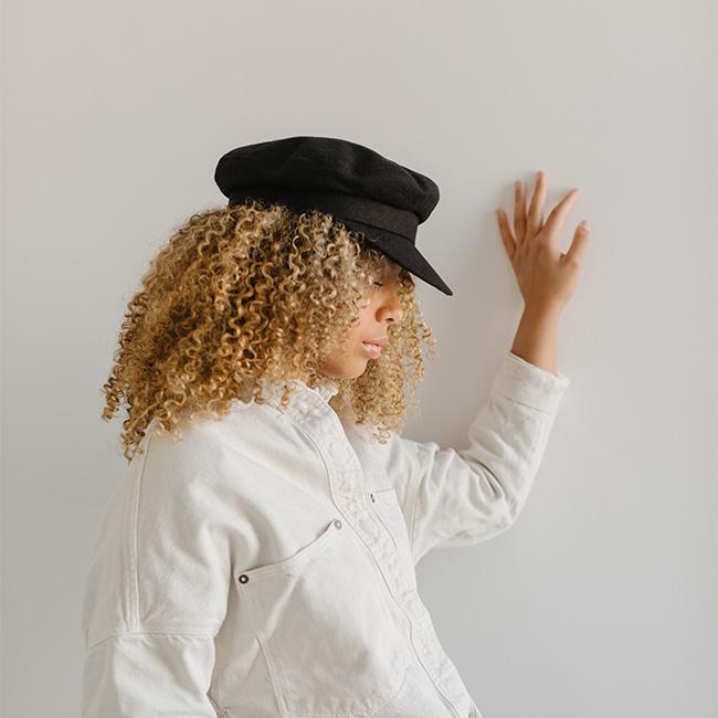 Woman wearing a black cap and a white shirt, facing sideways against a plain background #color_black