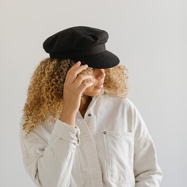 Woman wearing a black cap and a white shirt, posing sideways against a plain background #color_black