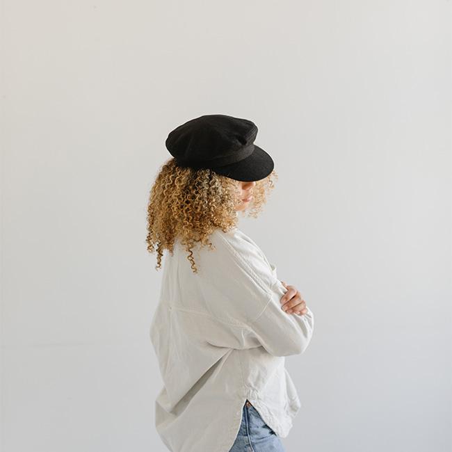 Woman wearing a black cap and a white shirt, facing sideways against a plain background #color_black