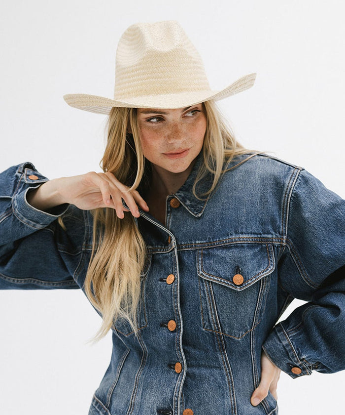 Woman wearing a natural colored straw cowboy hat and a denim shirt, posing against a plain background  #color_natural