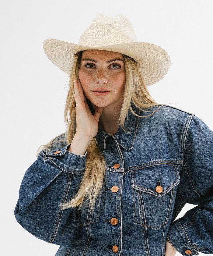 Woman wearing a natural colored straw cowboy hat and a denim shirt against a plain background  #color_natural