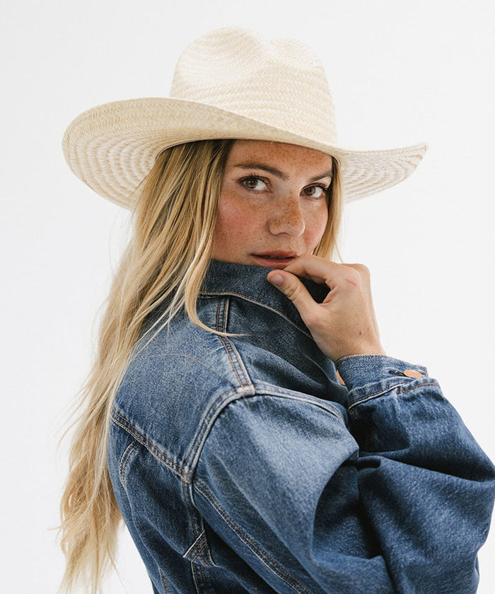 Woman wearing a natural colored straw cowboy hat and a denim shirt, posing sideways against a plain background  #color_natural