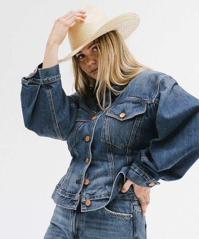 Woman wearing a natural colored straw cowboy hat, a denim shirt and blue jeans, posing against a plain background  #color_natural