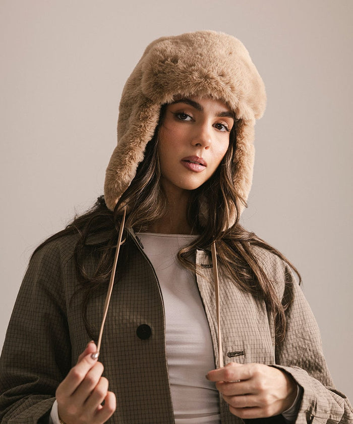 Woman wearing a fur-trimmed hat and coat against a plain background #color_tan