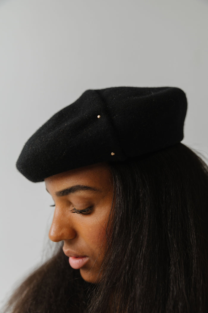 Woman wearing a black beret facing sideways against a plain background #color_black