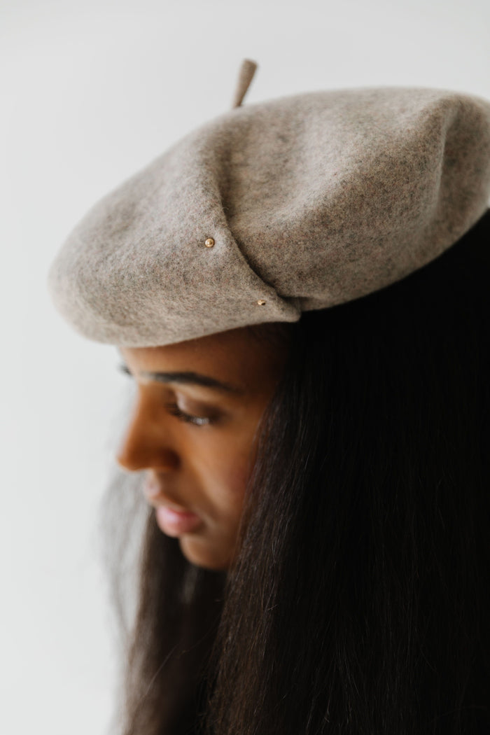Woman wearing a taupe beret facing sideways against a plain background  #color_taupe