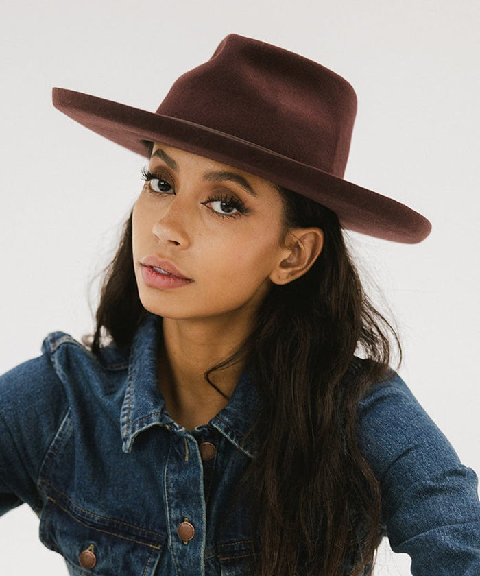 Woman wearing a dark cherry colored felt fedora hat and a denim shirt against a plain background #color_dark cherry