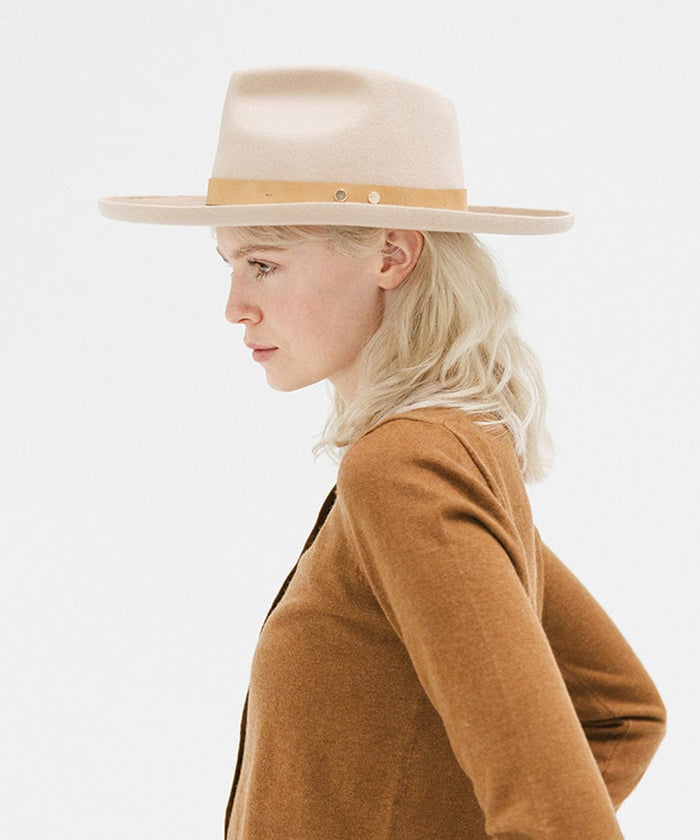 Woman wearing a cream felt fedora hat with a hat band and a brown sweater, looking sideways against a plain background  #color_cream