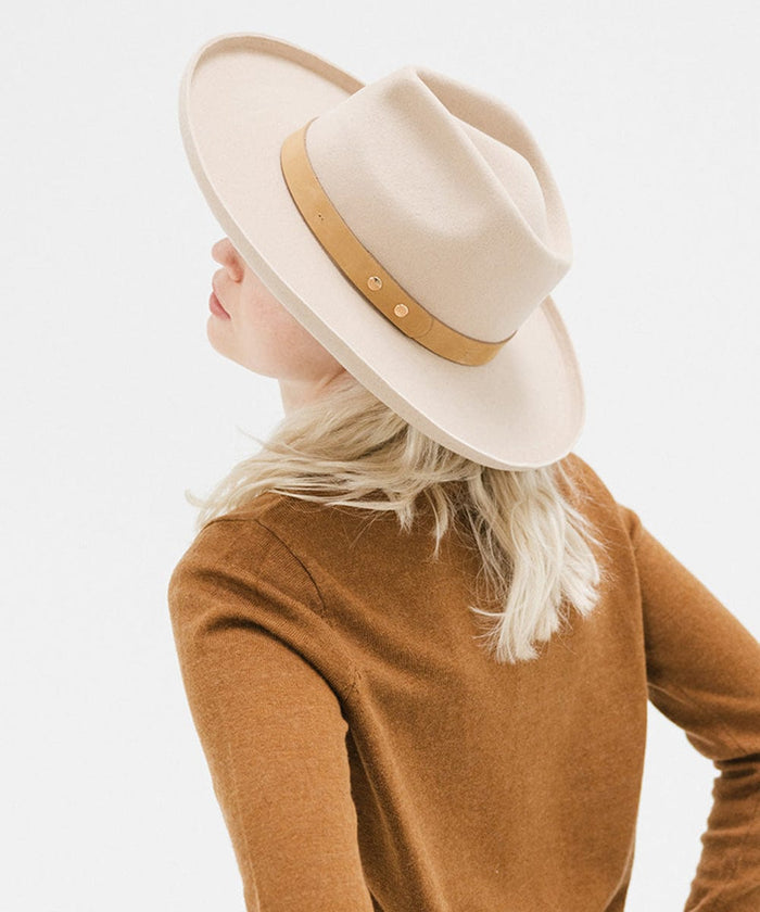 Woman wearing a cream felt fedora hat with a hat band and a brown sweater, facing behind against a plain background #color_cream