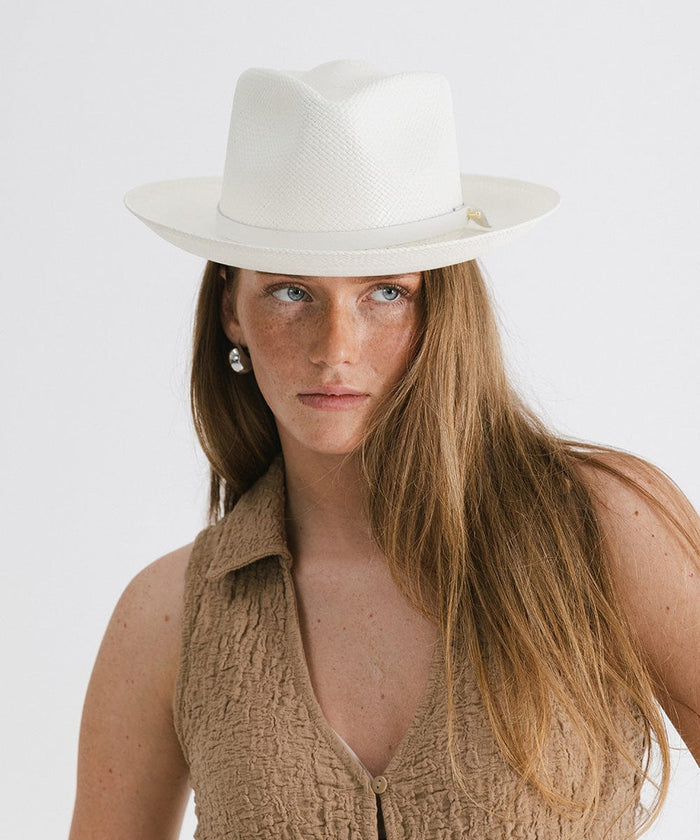 Woman wearing a white straw hat with a hat band and a brown top against a plain background  #color_white