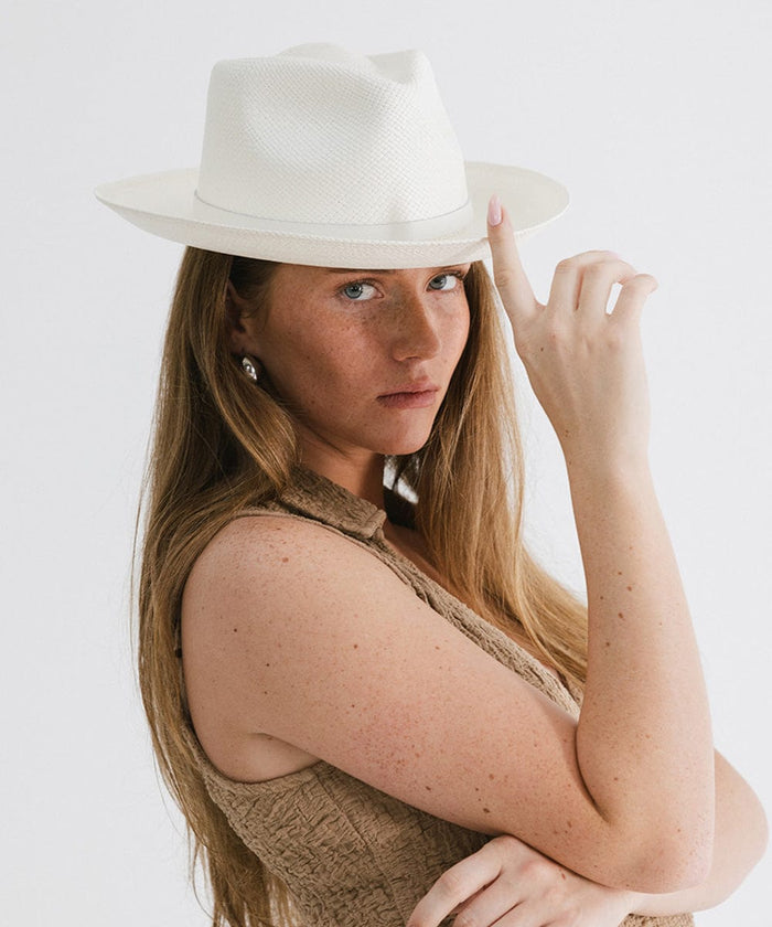 Woman wearing a white straw hat with a hat band and a brown top, posing sideways against a plain background  #color_white