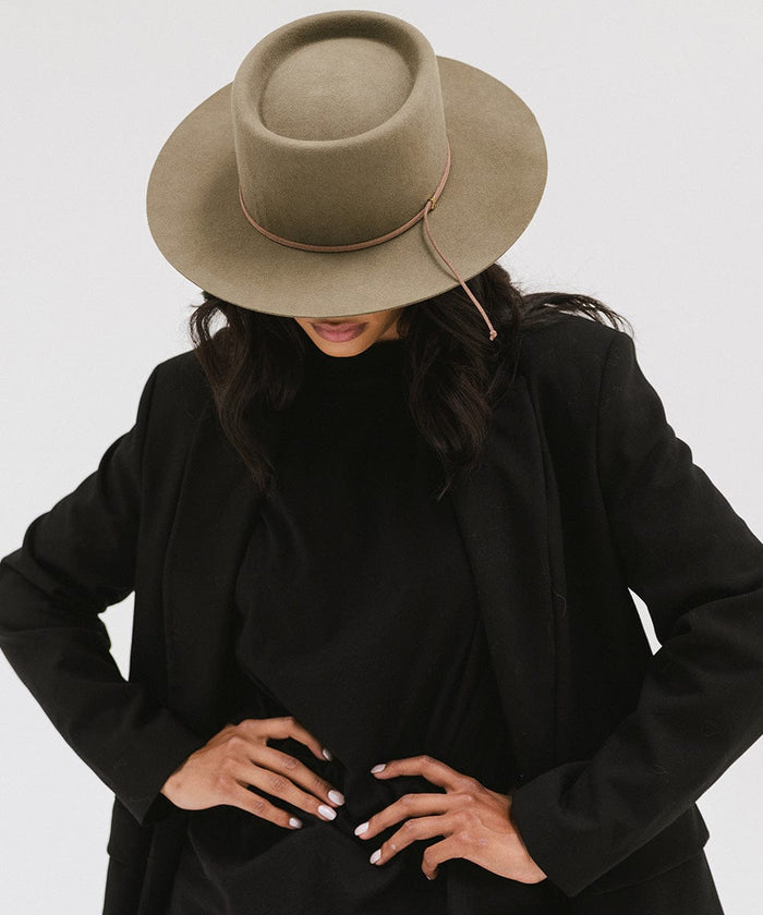 Woman wearing an aloe colored Maise classic flat brim hat with a hat band and a black t-shirt with a black blazer, posing against a plain background #color_aloe