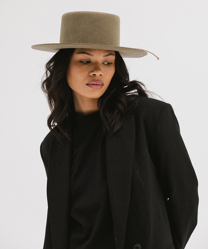 Woman wearing an aloe colored Maise classic flat brim hat and a black t-shirt with a black blazer against a plain background #color_aloe