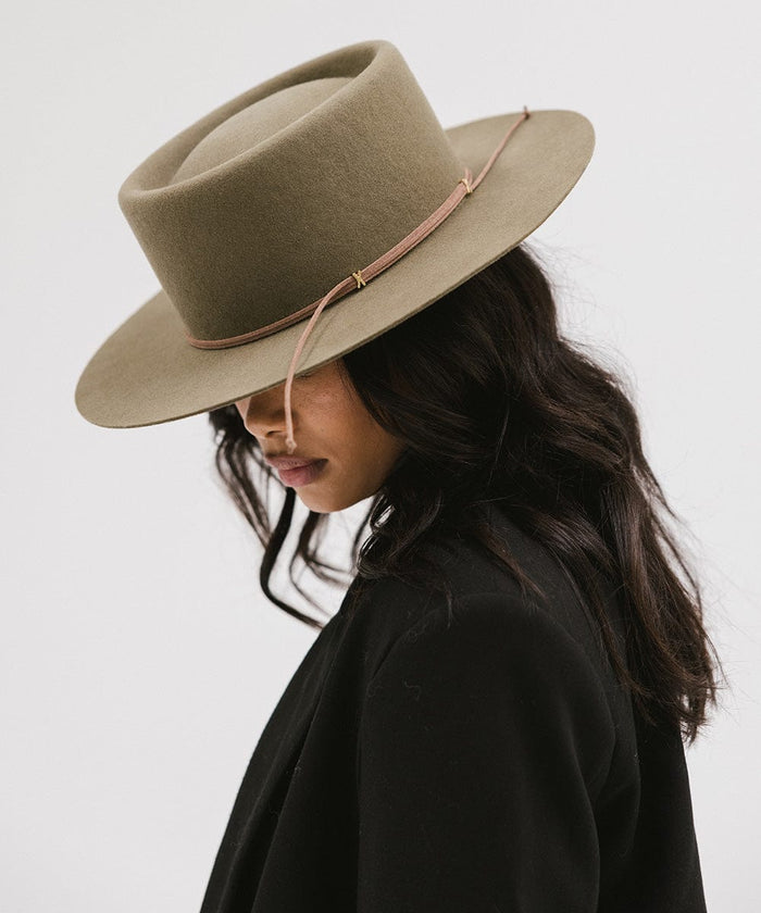 Woman wearing an aloe colored Maise classic flat brim hat with a hat band and a black blazer, posing sideways against a plain background #color_aloe