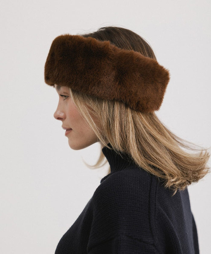 Woman wearing a brown fur headband and a black sweater, facing sideways against a plain background #color_brown