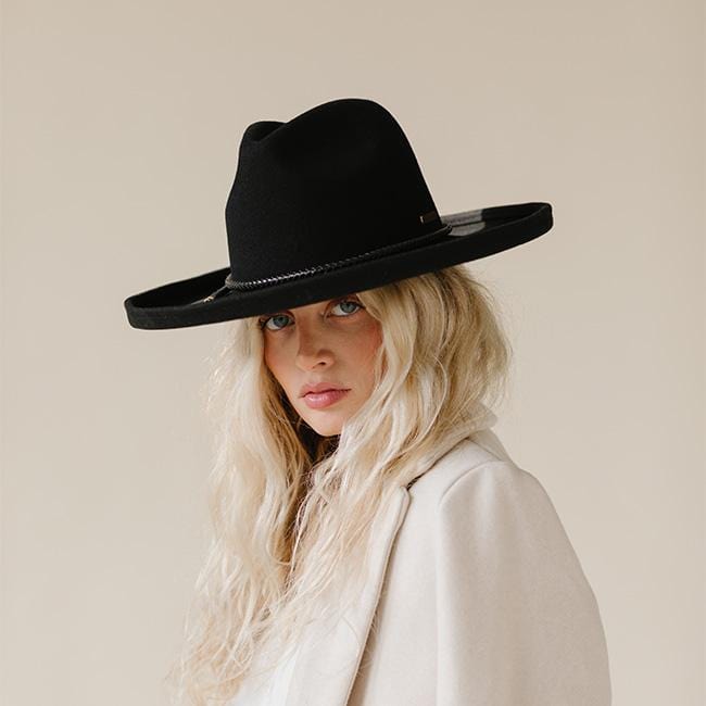 Woman wearing a black pencil brim felt hat with a hat band and a white blazer, posing against a plain background #color_black