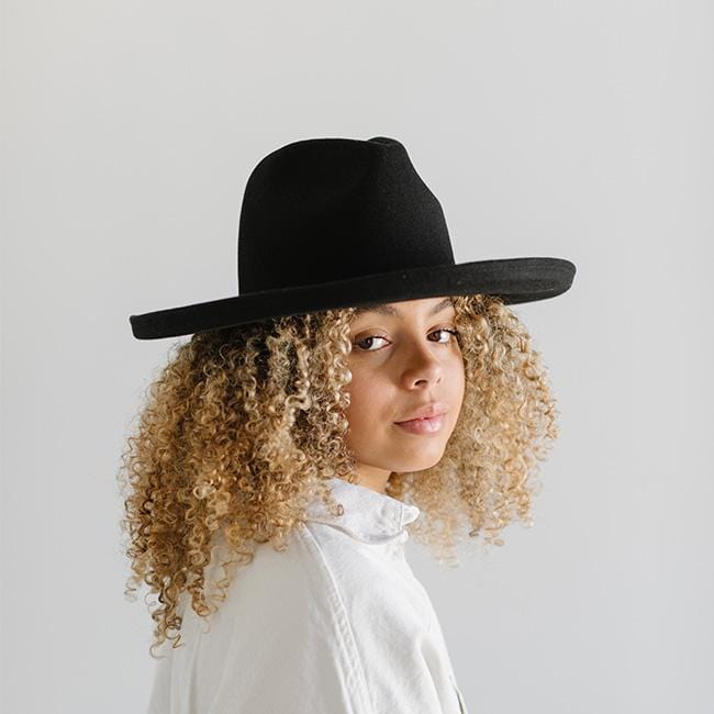 Woman wearing a black pencil brim felt hat and a white shirt against a plain background #color_black