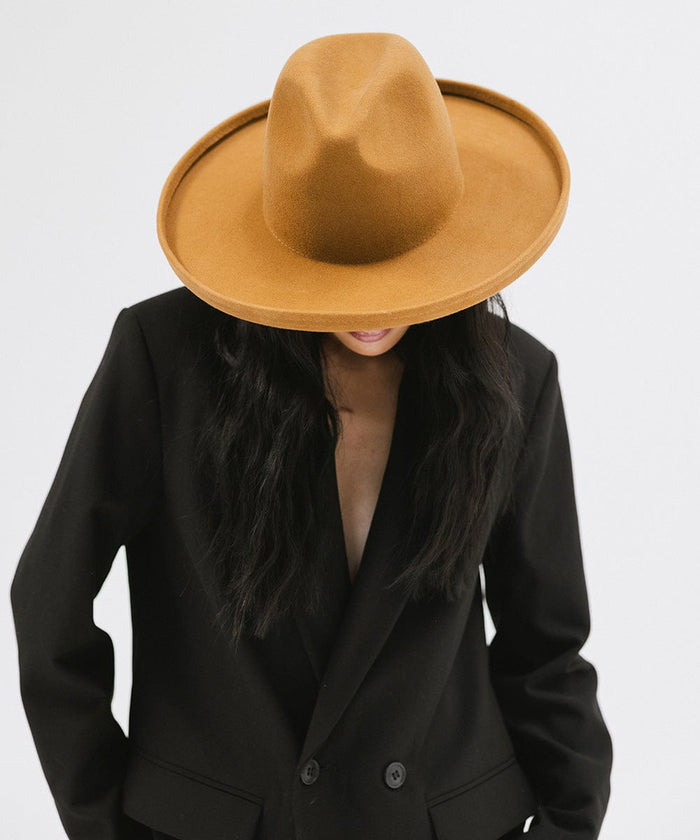Woman wearing a cinnamon colored  pencil brim felt fedora hat and a black blazer, looking down against a white background #color_cinnamon