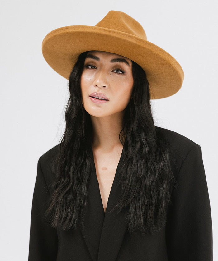 Woman wearing a cinnamon colored  pencil brim felt fedora hat and a black blazer against a white background #color_cinnamon