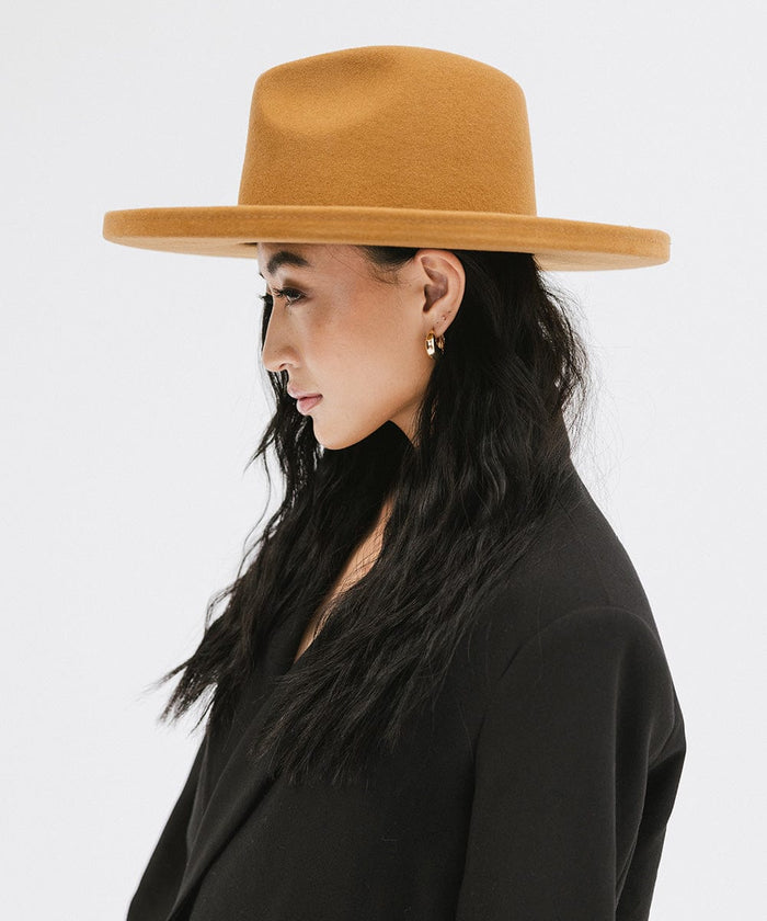 Woman wearing a cinnamon colored  pencil brim felt fedora hat and a black blazer, looking sideways against a white background #color_cinnamon