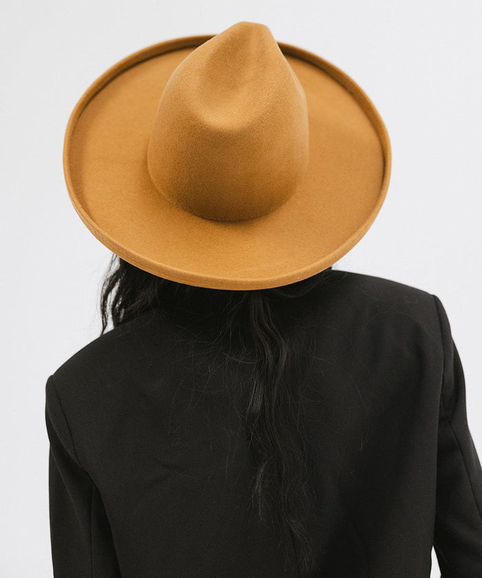 Woman wearing a cinnamon colored  pencil brim felt fedora hat and a black blazer, facing behind against a white background #color_cinnamon