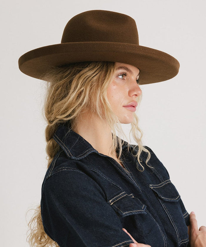 Woman wearing a chocolate colored pencil brim fedora hat and a denim shirt, facing sideways against a plain background #color_chocolate