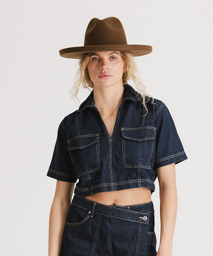 Woman wearing a chocolate colored pencil brim fedora hat, a denim shirt and a denim skirt against a plain background #color_chocolate