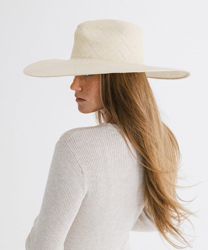 Woman with long hair wearing a natural colored wide brim straw hat and a white top, posing sideways against a plain background  #color_natural