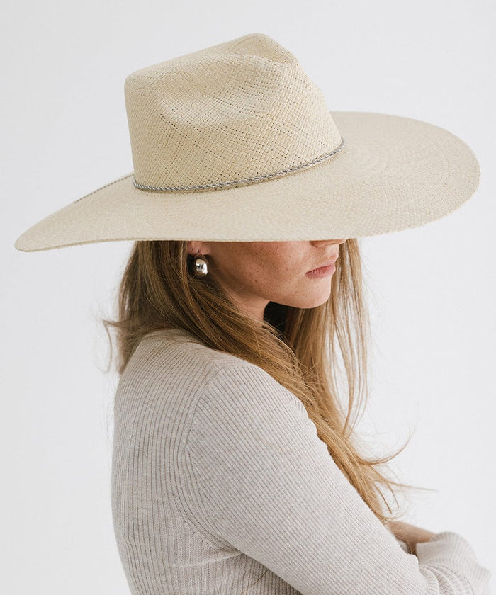 Woman wearing a natural colored wide brim straw hat and a white top, looking sideways against a plain background  #color_natural