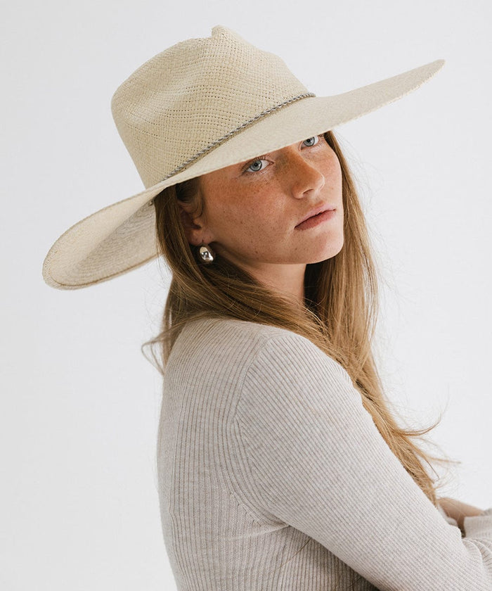 Woman wearing a natural colored wide brim straw hat and a white top against a plain background  #color_natural