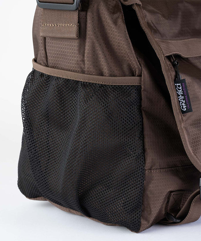 Close-up of a brown and black Gramicci Messenger Bag on a light tone background.