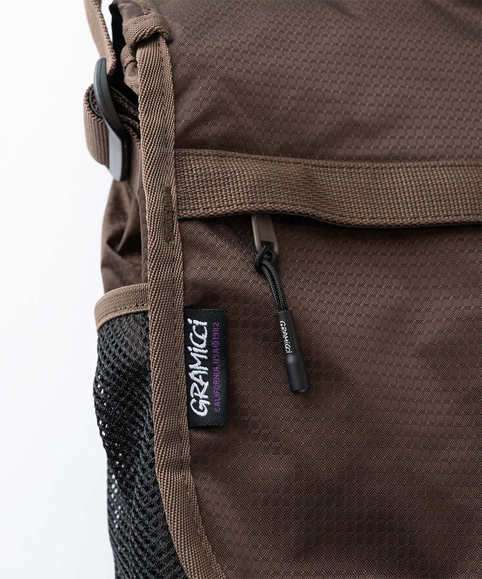 Close-up of a brown and black Gramicci Messenger Bag on a light tone background.
