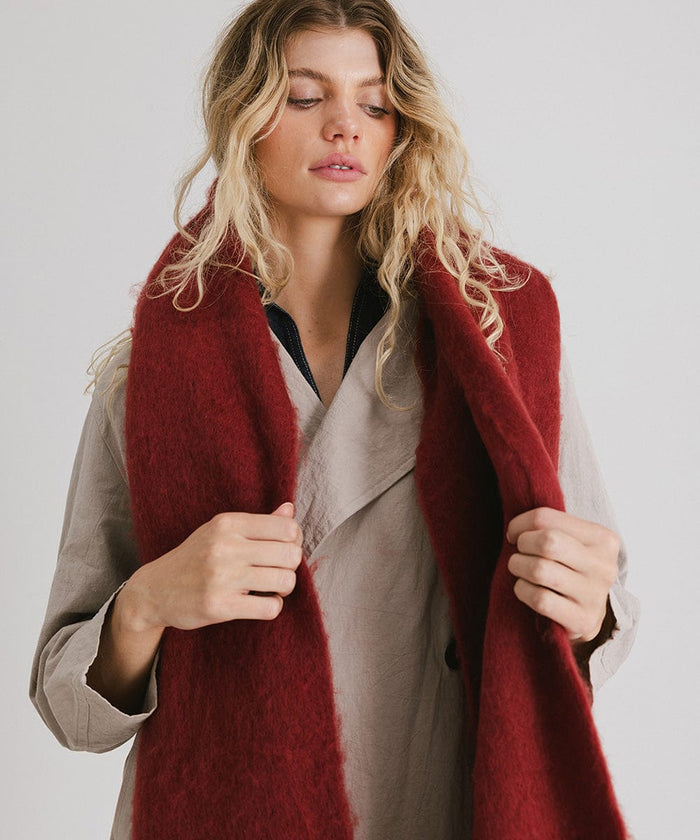 Woman wearing a burgundy oversized knit scarf with fringes, draped over the neck against a plain background #color_burgundy