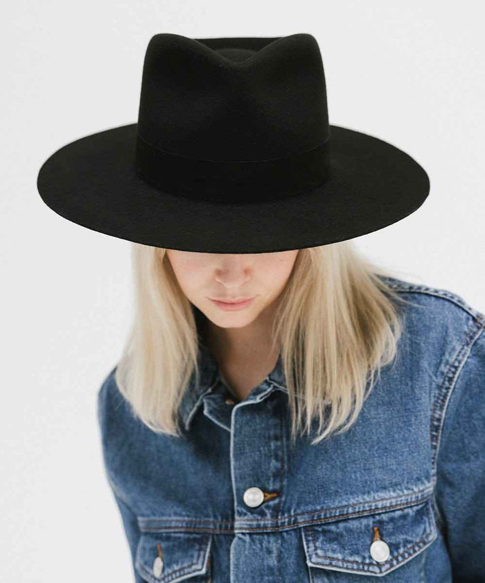 Person wearing a black fedora hat with a band and denim jacket, looking down against a white background #color_black