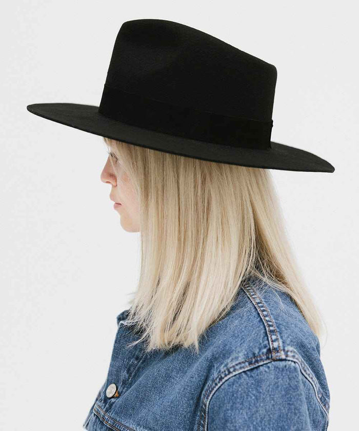 Person wearing a black fedora hat with a band and denim jacket, facing sideways against a white background #color_black