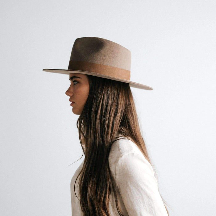 Woman wearing a brown fedora hat with a band and a white shirt, facing sideways against a plain background #color_brown