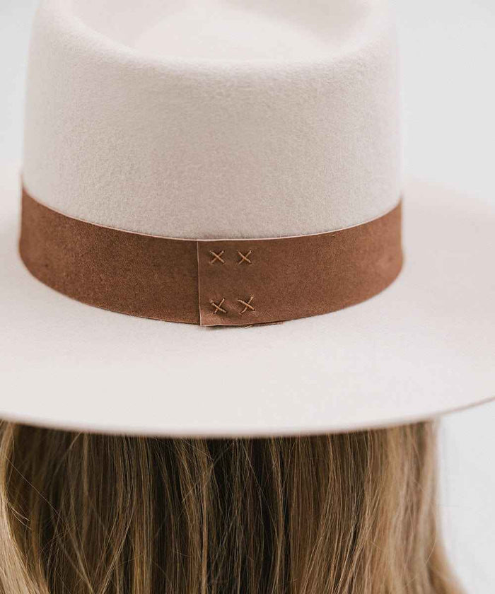 Ivory colored fedora hat with a brown band worn by a person with long hair. #color_ivory