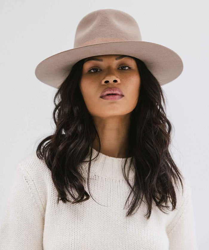 Woman wearing a brown fedora hat and white sweater against a plain background #color_brown