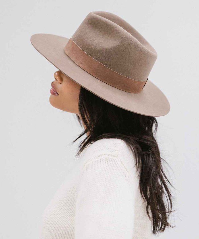 Woman wearing a brown fedora hat with a band with a brown band and a white sweater, facing sideways against a white background #color_brown
