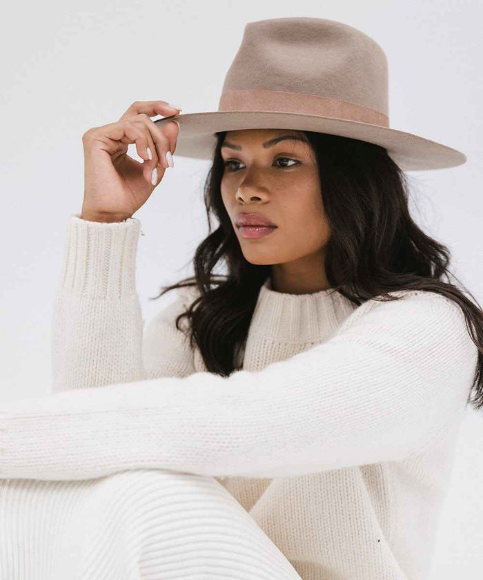 Woman wearing a brown fedora hat with a band and white sweater, posing against a plain background #color_brown