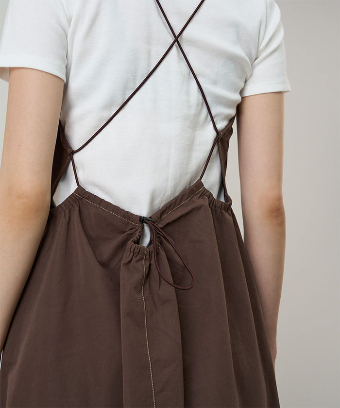Back view of a model wearing a Gramicci Women's Woven Milton Dress in the color walnut and a white undershirt on a light-tone background.