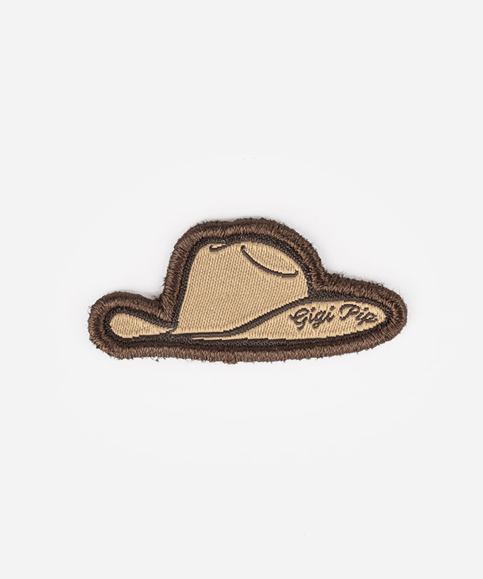 An embroidered patch shaped like a cowboy hat, featuring a tan center with a dark brown stitched border and script text reading 'Gigi Pipi' on the right side, set against a plain light gray background #color_tan