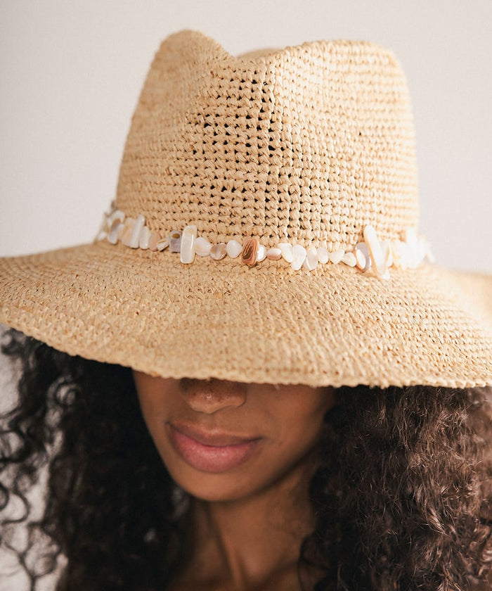 Woman wearing a straw hat with decorative shells on a plain background #color_natural
